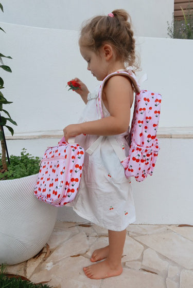 girl wearing cherry mini backpack and holding cherry mini lunch bag