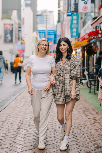 Two women walking hand-in-hand on a city street with colorful signs and buildings in the background.